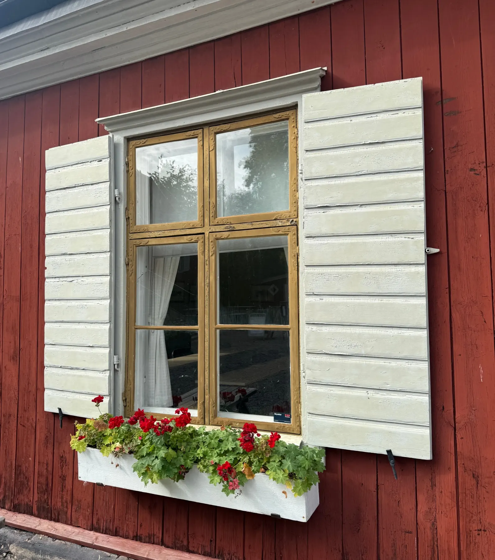 Renoverat träfönster med vita fönsterluckor på en röd fasad